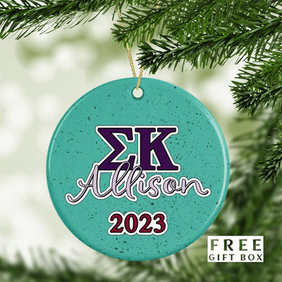 May include: A round, teal-colored Christmas ornament with white speckles. The ornament has a purple and white &#39;ΣΚ&#39; and the name &#39;Allison&#39; in white with a purple outline. The year &#39;2023&#39; is in red with a white outline. The ornament is hanging from a gold string.