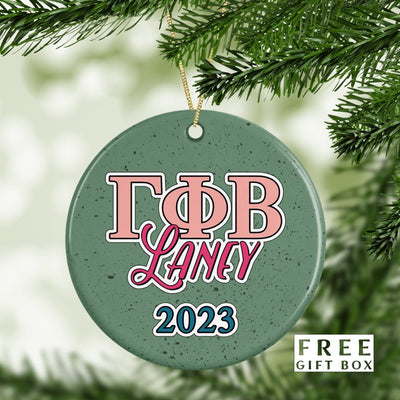 May include: A green ceramic Christmas ornament with white speckles. The ornament has pink and white letters that spell out &#39;ΓΦΒ Laney 2023&#39;.