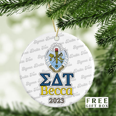 May include: A white round Christmas ornament with a blue and gold Sigma Delta Tau sorority crest and the text &#39;ΣΔΤ Becca 2023&#39; printed on it. The background of the ornament is covered with a repeating pattern of the words &#39;Sigma Delta Tau&#39;.