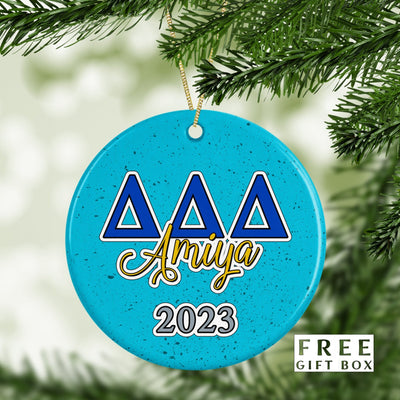 May include: A blue and white Christmas ornament with the letters &#39;ΔΔΔ&#39; in blue and the word &#39;Amiya&#39; in gold script. The year &#39;2023&#39; is written in gray below the name. The ornament has a speckled blue background.