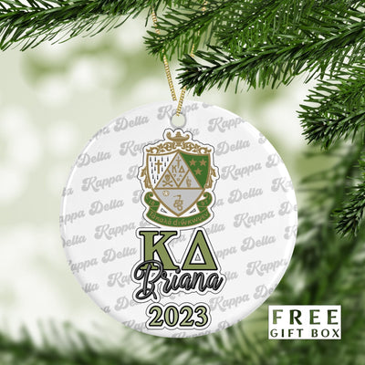 May include: A white round Christmas ornament with a green and gold Kappa Delta sorority crest. The ornament also has the letters &#39;KA&#39; in green and gold, the name &#39;Briana&#39; in black cursive, and the year &#39;2023&#39; in black. The ornament is surrounded by a repeating pattern of &#39;Kappa Delta&#39; in green and gold. The text &#39;FREE GIFT BOX&#39; is in the lower right corner of the image.