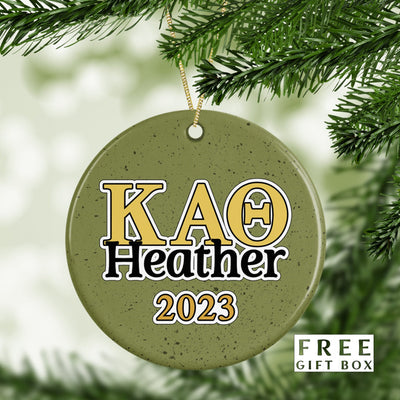 May include: A green round ceramic ornament with gold and black lettering. The ornament says &#39;KAO Heather 2023&#39;.