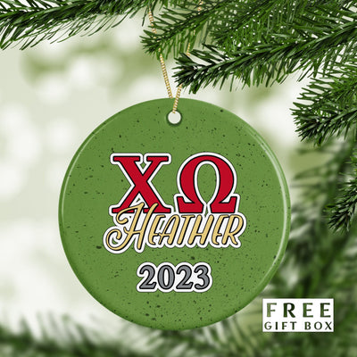 May include: A green round Christmas ornament with the letters XO in red and the Greek letter omega in red. The letters are outlined in white. Below the letters is the word &#39;HEATHER&#39; in gold script. Below the word &#39;HEATHER&#39; is the year &#39;2023&#39; in gray. The ornament has a speckled green background.