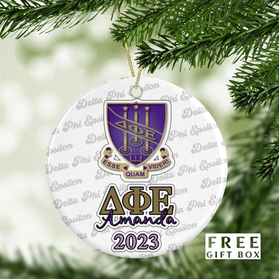 May include: A white round Christmas ornament with a purple and gold sorority crest, the letters &#39;ΔΦΕ&#39; in gold, the name &#39;Amanda&#39; in gold, and the year &#39;2023&#39; in purple. The ornament is surrounded by a repeating pattern of the words &#39;Delta Phi Epsilon&#39;.